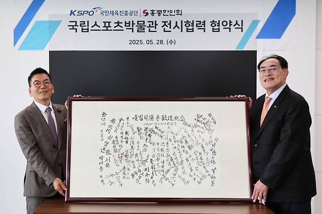 하형주 서울올림픽기념국민체육진흥공단 이사장(오른쪽)이 탁연균 홍콩한인회장으로부터 1948 런던올림픽 참가 선수단 서명문 액자를 받고 함께 들어올리면서 기념 촬영하고 있다. 국민체육진흥공단