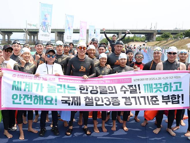 ‘쉬엄쉬엄 한강 3종 축제’ 1일차 수영종목 참가 전 시민들과 함께 ‘깨끗하고 안전한 수질을 자랑하는 한강’ 문구가 담긴 현수막을 들고 홍보활동을 펼치고 있다. [서울시 제공]