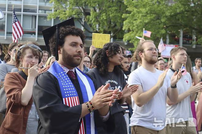 [캠브리지(매사추세츠)=AP/뉴시스] 도널드 트럼프 미국 행정부가 하버드대학에 한 달 뒤 외국인 학생 등록을 다시 차단하겠다고 했지만, 법원이 곧바로 제동을 걸었다고 29일(현지 시간) 미국 언론이 보도했다. 사진은 하버드대 졸업생인 빅터 플로레스를 비롯한 학생들이 지난 27일 교내에서 열린 반트럼프 시위에서 한 학생의 연설에 박수를 치는 모습. 2025.05.30.