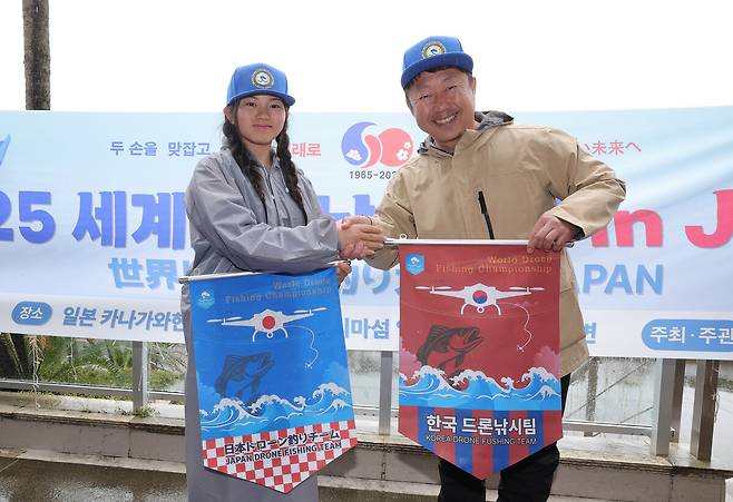 김청연 한국 참가자 대표(왼쪽)와 와치 슈고 일본 참가자 대표가 ‘2025 세계드론낚시대회 in Japan’ 기념 깃발을 교환하고 있다.가마쿠라=이재문 기자