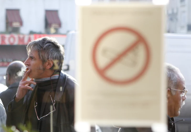 금연 로고 뒤로 흡연 중인 시민. [사진 = 로이터]