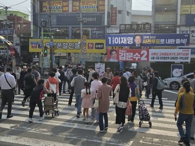 부산 시민들이 이재명·김문수 대선 후보 플래카드 앞 횡단보도를 건너는 모습./사진=유재희 기자.