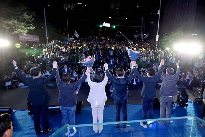 제21대 대통령 당선이 확실시되는 더불어민주당 이재명 대선 후보와 부인 김혜경 여사가 4일 서울 여의도 국회 인근에서 당 주최로 열린 국민개표방송 행사에 참석해 박찬대 상임총괄선대위원장과 정은경 총괄선대위원장단으로부터 꽃다발을 받은 뒤 시민들을 향해 두 팔을 들어 인사하고 있다 [공동취재] 연합뉴스