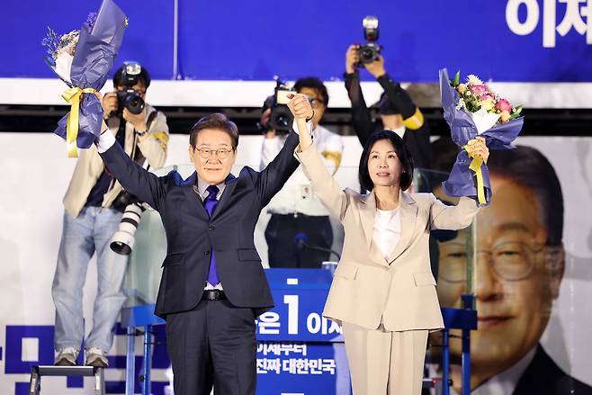 Lee Jae-myung, who is all but certain to be elected president,  and his wife Kim Hye-kyung greet supporters with raised arms after receiving bouquets during a public vote-count event hosted by the party near the National Assembly in Yeouido, Seoul, on Wednesday. (Pool Photo via Yonhap)