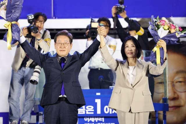 ▲ 제21대 대통령 당선이 확실시되는 더불어민주당 이재명 대선 후보와 부인 김혜경 씨가 4일 서울 여의도 국회 인근에서 당 주최로 열린 국민개표방송 행사에 참석해 꽃다발을 받고서 시민들을 향해 두 팔을 들어올려 인사하고 있다. ⓒ연합뉴스