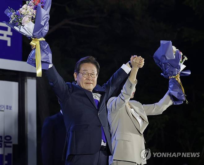 시민들 향해 인사하는 이재명 후보 내외 (서울=연합뉴스) 김주성 기자 = 제21대 대통령 당선이 확실시되는 더불어민주당 이재명 대선 후보와 부인 김혜경 여사가 4일 서울 여의도 국회 인근에서 당 주최로 열린 국민개표방송 행사에 참석해 꽃다발을 받고서 시민들을 향해 두 팔을 들어 인사하고 있다. 2025.6.4 [공동취재] utzza@yna.co.kr