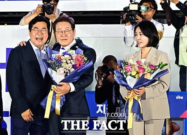 이재명 대통령이 4일 서울 영등포구 여의도 글래드호텔 앞에 마련된 민주당 개표방송 야외무대에서 꽃다발을 들고 박찬대 상임총괄선대위원장의 어깨에 손을 올리며 기념 촬영을 하는 모습. 오른쪽은 이 대통령 부인 김혜경 여사. /배정한 기자