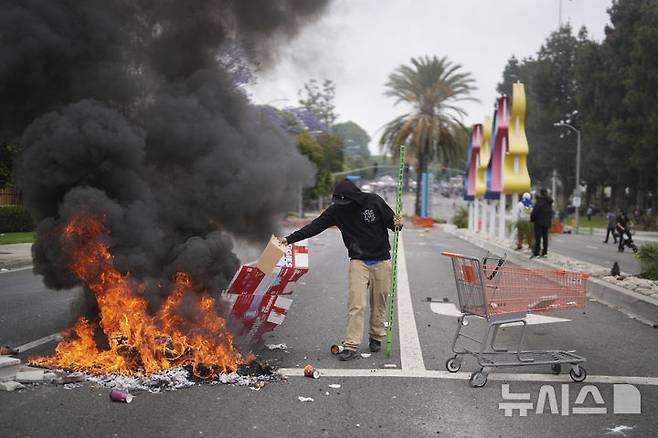 [캘리포니아=AP/뉴시스] 도널드 트럼프 미국 대통령이 이민 단속 시위를 진압하기 위해 캘리포니아주에 주방위군 2000명을 투입하라고 지시하자 "극히 이례적인 조치"라는 평가가 나오고 있다고 뉴욕타임스가 8일(현지 시간) 보도했다. 사진은 7일 캘리포니아 파라모운트의 한 산업 단지 밖에서 방호복과 가스 마스크를 착용한 국경 순찰대 요원들이 경계를 서고 있는 가운데, 한 시위자가 불길에 잡동사니를 넣고 있다. 2025.06.08.