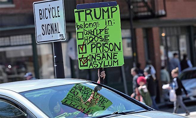 한 운전자가 2025년 4월 17일, 미국 매사추세츠주 케임브리지의 하버드대에서 열린 트럼프 행정부의 학생 비자 취소 조치에 반대하는 시위 후, 하버드 스퀘어에서  손 팻말을 들고 있다.  /로이터연합