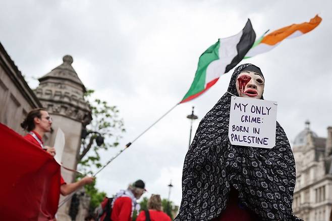 2025년 6월4일 영국 런던의 웨스트민스터 하원 의사당 부근에서 열린 집회에서 가면을 쓴 한 참가자의 목에 ‘내 유일한 죄: 팔레스타인에서 태어난 것’이라고 적힌 팻말이 걸려 있다. AFP 연합뉴스