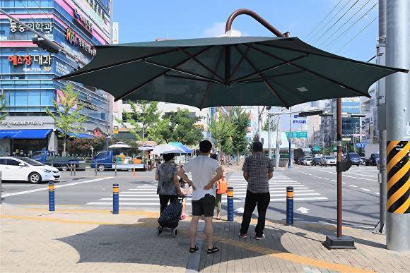 무더운 폭염 속, 다사읍 대실역 인근에 설치된 그늘막 아래서 행인들이 횡단보도 신호를 기다리며 더위를 피하고 있다 [사진=달성군]