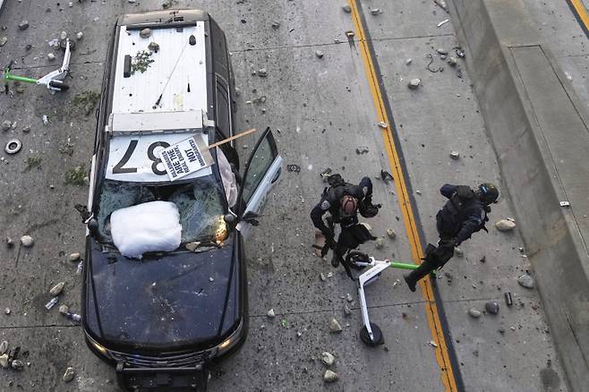 캘리포니아 고속도로 순찰대 경찰관 두 명이 8일(현지시간) 로스앤젤레스 도심 메트로폴리탄 구치소 인근에서 불법이민 단속 반대 시위대들이 던지는 돌멩이를 피하고 있다.