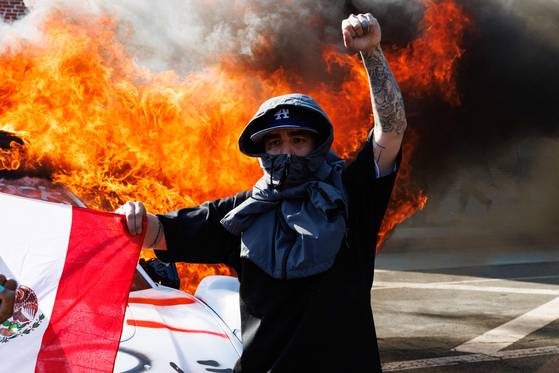 지난 8일 미국 캘리포니아주 로스앤젤레스에서 한 시위자가 멕시코 국기를 들고 주먹을 치켜든 채 불타고 있는 차량 앞에 서있다. AFP=연합뉴스