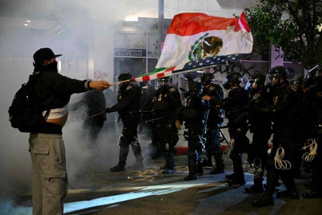 9일 밤 미국 캘리포니아주 로스앤젤레스 도심에서 열린 불법 이민 단속 반대 시위에서 한 시위자가 진압 장비를 갖춘 경찰 앞에서 멕시코와 미국 국기를 흔들고 있다. 로스앤젤레스