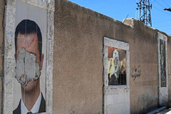 축출된 시리아 대통령 바샤르 알 아사드(왼쪽)와 그의 아버지 하페즈 알 아사드(가운데)의 훼손된 초상화가 2일(현지시간) 수도 다마스쿠스의 벽에 걸려 있다.AFP=연합뉴스