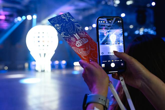 A fan photographs a balloon-shaped light installation at "Army Bomb Photo Spot" while holding a 2025 BTS Festa ticket at Kintex in Goyang, Gyeonggi Province, Friday. (Big Hit Music)
