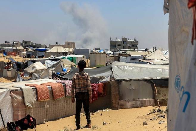 2025년 6월11일 팔레스타인 땅 가자지구 최남단 라파의 피란민촌에서 한 어린이가 이스라엘군 공습으로 뿌연 연기가 피어오르는 모습을 바라보고 있다. AFP 연합뉴스