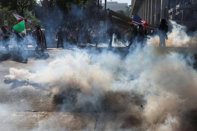 14일 미국 캘리포니아주 로스앤젤레스 연방 청사 앞에서 경찰들이 시위자들을 해산시키기 위해 최루가스를 분사하고 있다. 로스앤젤레스=로이터 연합뉴스