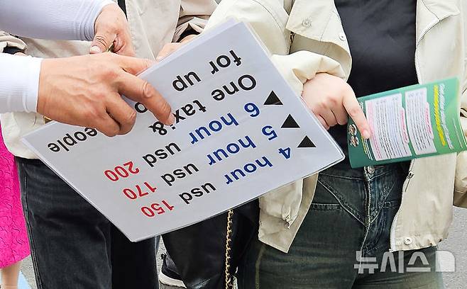 [제주=뉴시스] 우장호 기자 = 18일 오전 서귀포강정크루즈터미널 출국장 입구에서 택시기사들이 영어로 표기된 가격표를 손에 들고 외국인 관광객을 상대로 호객 행위를 하고 있다. 2025.06.18. woo1223@newsis.com