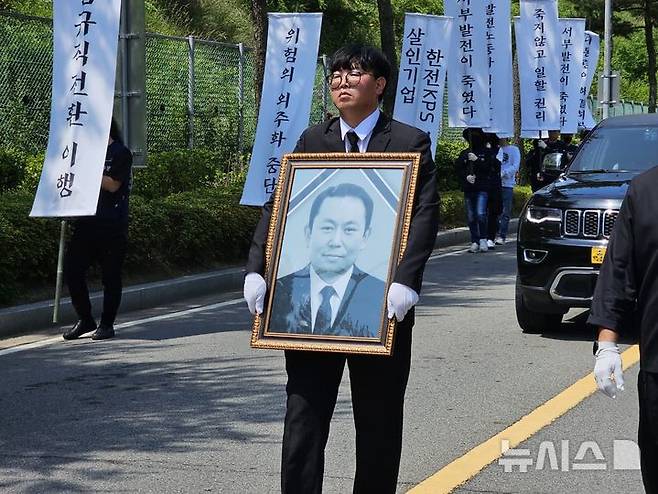 [태안=뉴시스] 김덕진 기자=김영훈 한전KPS비정규직지회 회장이 18일 오전 고 김충현씨 영정 사진을 들고 생정 그가 일했던 태안화력발전소 한전KPS 태안사무처 건물로 이동하고 있다. 2025.06.18. spark@newsis.com