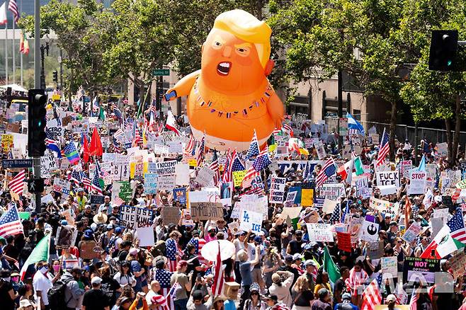 [로스앤젤레스=AP/뉴시스]  미 캘리포니아주 로스앤젤레스에서 6월 14일 트럼프의 제왕적 국정운영을 비난하는  ‘노 킹스(No Kings)’ 시위 참가자들이 각종 손팻말을 들고 행진하고 있다.  미 UCLA대학의 올 여름 경제전망 보고서는 캘리포니아 경제가 트럼프 관세정책과 이민추방, 진압군 투입 여파로 하반기에 퇴락할 것을 예고했다.  2025.06.19.