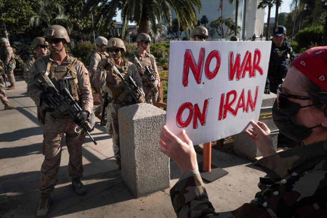 지난 18일 미국 캘리포니아주 로스앤젤레스의 연방 청사 단지를 해병대원들이 경비하고 있는 가운데, 한 시위자가 이란과의 전쟁에 반대하는 팻말을 들고 있다. 로스앤젤레스=AFP 연합뉴스