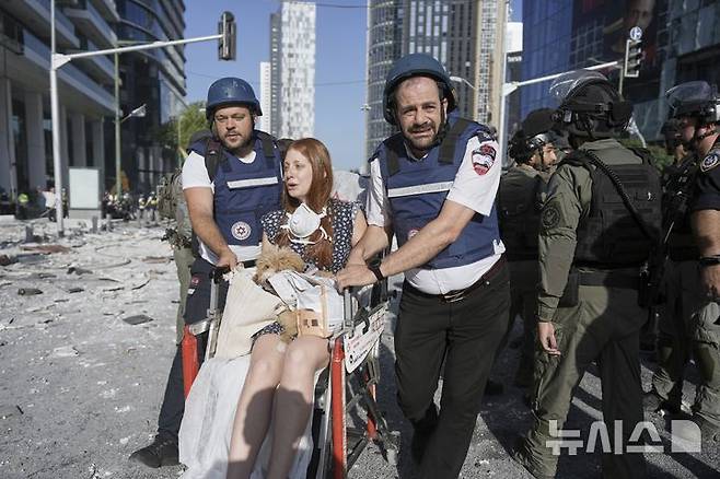 [라마트간=AP/뉴시스] 19일(현지 시간) 이스라엘 텔아비브 인근 라마트간에서 이란의 미사일 직격으로 부상한 여성이 구조대의 도움을 받으며 대피하고 있다. 2025.06.20.