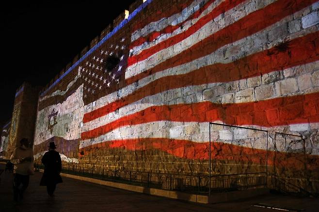 22일(현지시간) 이스라엘 예루살렘 구시가지에서 이스라엘 국기와 미국 국기가 비친친 벽을 사람들이 지나고 있다. AFP연합뉴스