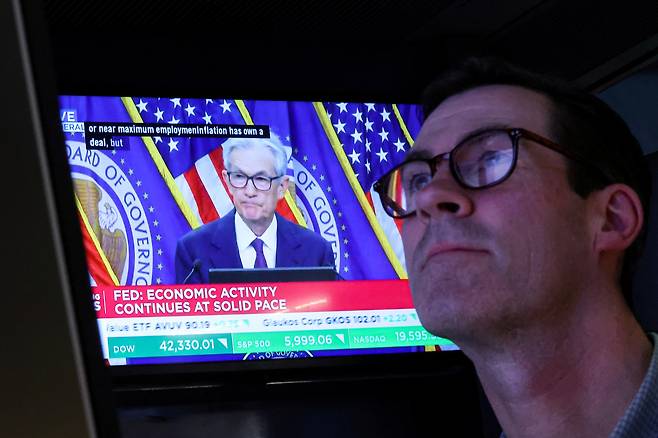 미국 뉴욕증권거래소(NYSE)에서 미국 연방준비제도이사회(Fed) 의장 제롬 파월이 연방준비제도이사회 금리를 발표한 후 기자회견을 하는 모습이 화면에 나오는 가운데, 한 거래자가 작업하고 있다. [로이터]