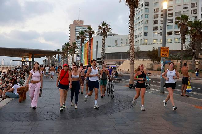 22일(현지시간) 이란과 이스라엘 무력 충돌이 10일째 이어지는 가운데, 시민들이 이스라엘 텔아비브 해변 산책로를 따라 조깅을 하고 있다. [AFP]