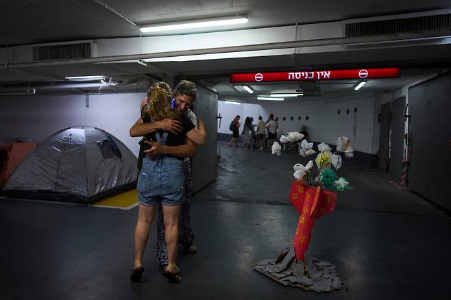 23일 이스라엘 텔아비브의 방공 시설로 사용되는 지하 주차장에서 한 남녀가 포옹하고 있다. 옆에는 이란과의 무력 충돌에 따른 사상자를 추모하는 꽃이 로켓 모양의 용기에 담겨 놓여 있다./로이터 연합뉴스