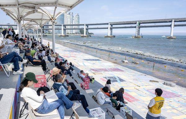 지난 15일 부산 수영구 민락수변공원 일원에서 ‘2025 부산바다도서관’이 열린 가운데 시민들이 그늘 아래에서 시원한 바닷바람을 맞으며 책을 읽고 있다.   국제신문DB