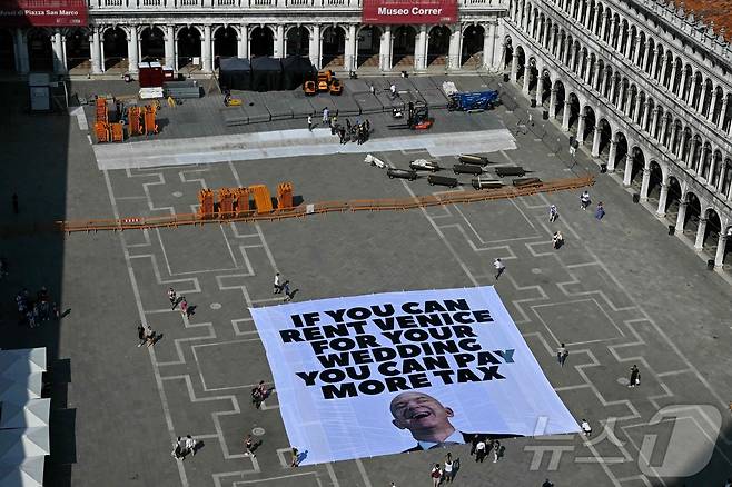 23일(현지시간) 국제 환경단체 그린피스 활동가들이 이탈리아 베네치아의 산 마르코 광장에서 제프 베이조스의 사진과 함께 "당신이 결혼식 장소로 베네치아를 빌릴 수 있다면 더 많은 세금을 내야 한다"는 문구가 적힌 대형 현수막을 설치하고 있다. 베네치아에서는는 이달 말 아마존 창업자 겸 CEO 제프 베조스와 언론인 로렌 산체스의 결혼식을 열릴 예정이며, 200명 이상의 하객이 참석할 것으로 예상된다. 25.06.23 ⓒ AFP=뉴스1 ⓒ News1 김예슬 기자