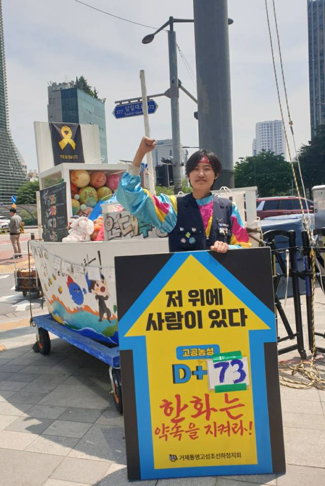 ▲인터뷰 당일(5월 26일) 거통고지회 농성장 앞 '연대투쟁호'를 배경으로 선 예은 씨. 바로 뒤에 보이는 회색 기둥이 김형수 지회장이 올라간 30m 철탑이다. ⓒ 임은경