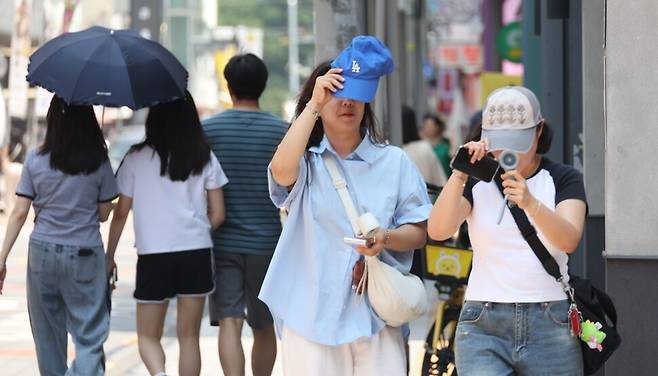 도심 거리에서 햇볕을 피하기 위해 모자와 선풍기를 사용하는 시민들