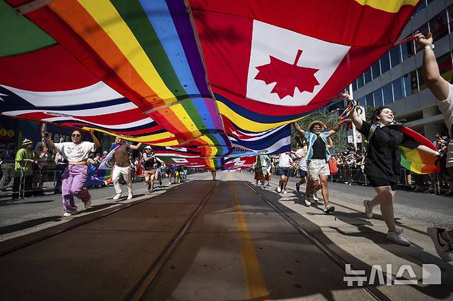 [토론토=AP/뉴시스] 29일(현지 시간) 캐나다 온타리오주 토론토에서 열린 프라이드 퍼레이드 참가자들이 대형 깃발을 들고 행진하고 있다. 매년 6월은 '세계 성소수자 프라이드의 달'로 세계 곳곳에서 기념행사가 열린다. 2025.06.30.