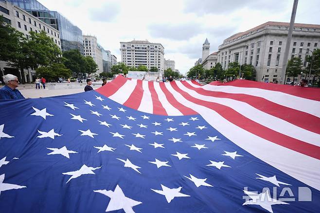 [워싱턴=AP/뉴시스] 지난 14일 미국 워싱턴 자유의 광장에서 시민들이 미 육군 창설 250주년 기념 열병식이 열리기에 앞서 대형 성조기를 펼쳐 들고 있다. 이날은 도널드 트럼프 대통령의 79번째 생일이기도 하다. 2025.06.15.