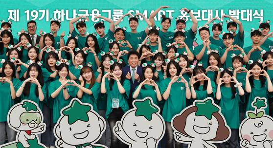 Hana Financial Group Chairman Ham Young-joo, center in second row, and Vice Chairman Lee Eun-hyung, second from left in the last row, pose with newly appointed SMART public relations ambassadors during an inauguration ceremony at the group's auditorium in Myeong-dong, central Seoul, on July 1.[HANA FINANCIAL GROUP]