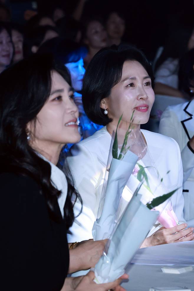 이재명 대통령의 배우자 김혜경 여사가 1일 서울 중구 신라호텔 다이너스티홀에서 열린 제4회 여성기업주간 개막식에 참석해 어린이 합창단원에게 받은 꽃을 들고 축하 공연을 보고 있다. 왼쪽은 이부진 호텔신라 사장. [연합]