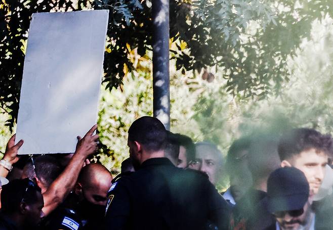 베냐민 네타냐후 이스라엘 총리(가운데 피켓을 보고 있는 사람)가 3일(현지시각) 이스라엘 남부 키부츠 니르오즈를 방문했다. 가자지구에 억류된 주민 이츠하크 엘가랏의 사진 피켓을 동생이 들어올리며 네타냐후 총리에게 인질 석방 협상을 촉구하고 있다. 니르오즈/로이터 연합뉴스