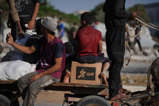 지난달 26일 가자지구 남부 칸유니스에서 팔레스타인 주민들이 가자인도주의재단(GHF)으로부터 구호품을 받아 나르고 있다. 칸유니스=AP 뉴시스