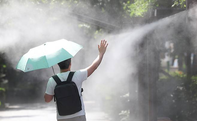 지난달 30일 대구 중구 국채보상운동기념공원에 쿨링포그(안개형 냉각수)가 가동 중인 가운데 한 시민이 양산을 들고 이동하고 있다. 연합뉴스 제공