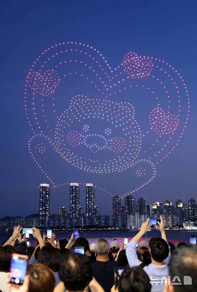 [부산=뉴시스] 하경민 기자 = 폭염특보와 열대야 현상으로 인해 밤낮으로 푹푹 찌는 더위가 이어진 5일 밤 부산 수영구 광안리해수욕장을 찾은 시민과 관광객들이 드론쇼를 구경하고 있다. 2025.07.06. yulnetphoto@newsis.com