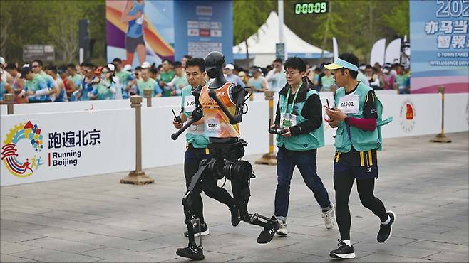 지난 4월 19일 중국 베이징에서 열린 휴머노이드 로봇 하프마라톤 대회에서 한 로봇이 기술 개발자들과 함께 달리고 있다. (EPA=연합뉴스)