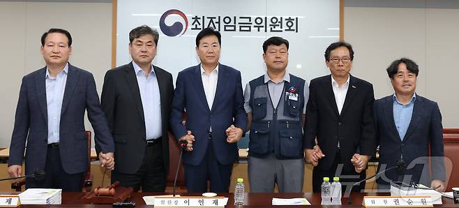 10일 저녁 세종시 정부세종청사 고용노동부에서 열린 최저임금위원회 제12차 전원회의에서 사용자위원과 한국노총 근로자위원들만이 참여하여 2026년 최저임금을 10,320원으로 합의하며 이인재위원장,류기정 사용자위원, 류기섭 근로자위원, 권순원 공익위원이 등이 손을 잡고 기념촬영을 하고 있다. 2025.7.10/뉴스1 ⓒ News1 김기남 기자