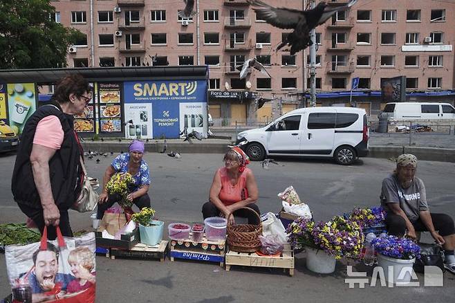[키이우=AP/뉴시스] 지난 10일(현지 시간) 우크라이나 키이우에서 여성들이 러시아의 공격으로 피해를 입은 건물 인근 노상에서 꽃과 라즈베리를 팔고 있다. 2025.07.12.