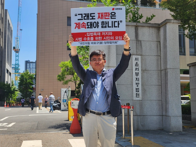 함운경 국민의힘 서울 마포을 당협위원장이 지난 6월11일 서울 마포구 소재 서울서부지법 앞에서 “그래도 재판은 계속돼야 합니다”라고 적힌 피켓을 들고 1인 시위를 하고 있다. 대통령 불소추특권에 대한 명확한 헌법 해석 없이 각 재판부가 이재명 대통령의 당선 전 형사재판들을 무기한 연기하자 항의하는 취지다. 함 당협위원장은 같은 전향 운동권 출신 민경우 시민단체 길 대표와 협력해 전국 각지에서 1인 시위를 벌이고 있다.<함운경 페이스북 사진>
