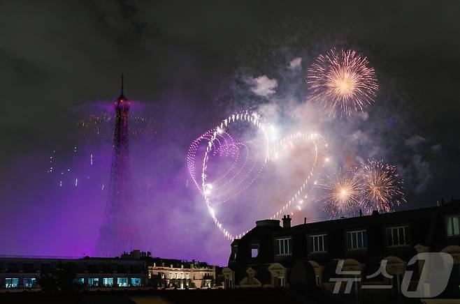 14일(현지시간) 프랑스 혁명 기념일(바스티유 데이)을 기념하기 위해 에펠탑에 펼쳐진 불꽃놀이 쇼에서 하트의 모양을 연출한 1천100대의 드론이 불꽃과 함께 빛의 향연을 펼치고 있다. 2024.7.15/뉴스1 ⓒ News1 이준성 기자