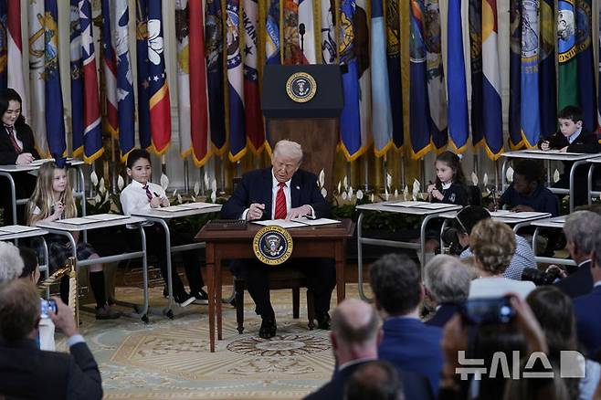 [워싱턴=AP/뉴시스] 도널드 트럼프 미국 대통령이 3월 20일 백악관 이스트룸에서 교육부 폐지를 위한 행정명령에 서명하고 있다. 트럼프 대통령은 교육을 다시 각 주(州)로 돌려보내겠다고 밝혔다. 그가 서명하는 뒤에서 학생들이 책상에 앉아 함께 서명하는 모습을 보이게 했다. 교육부폐지는 법원에 의해 제지 당했지만  미 20여개주는 트럼프의 교육지원금 동결을 이유로 7월 14일 교육부를 고소했다. 2025.07.15.