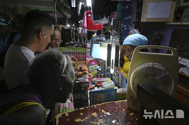 [하바나=AP/뉴시스] 15일(현지 시간) 쿠바 하바나에서 한 상인이 가게에 정전이 발생하자 충전식 램프 조명을 켠 채 고객에게 물건을 판매하고 있다. 2025.07.16.